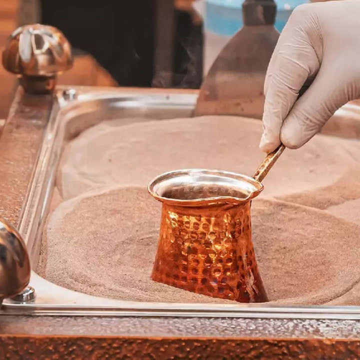 Hand holding copper decorative pot with sand on display table