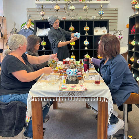 Instructor demonstrating mosaic lamp craft to workshop participants around a decorated table