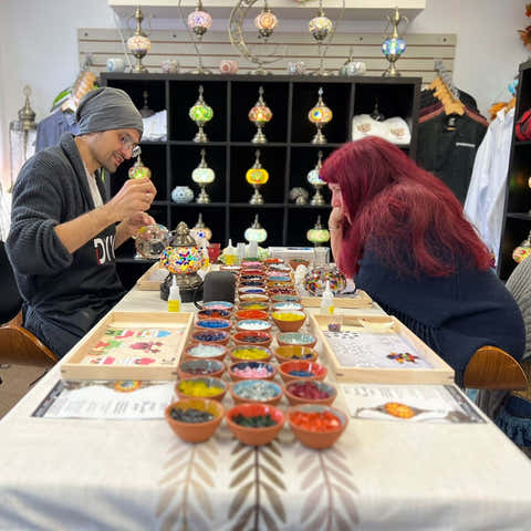 Instructor demonstrating mosaic lamp craft to workshop participants around a decorated table