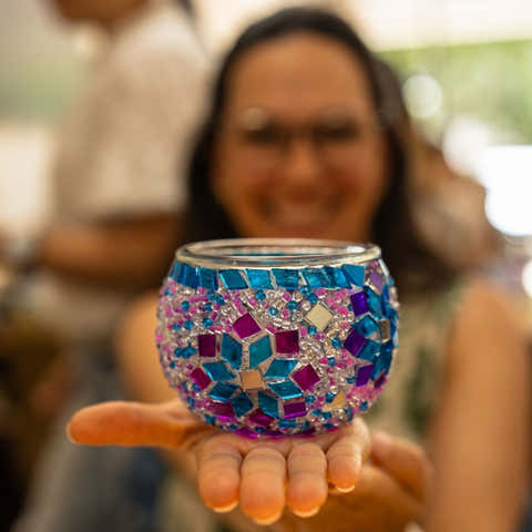 Person holding a colorful mosaic candle holder with blue, pink, and purple tiles and silver accents
